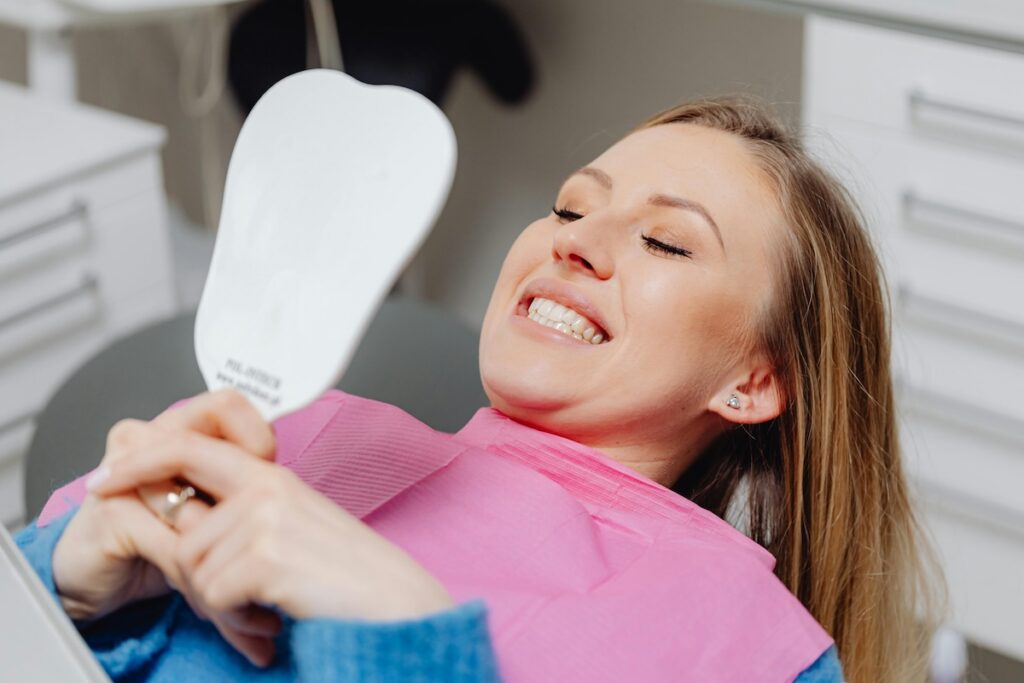 Smiling woman in dental chair holding a tooth-shaped mirror, admiring her teeth whitening results at Wisconsin Family Dental